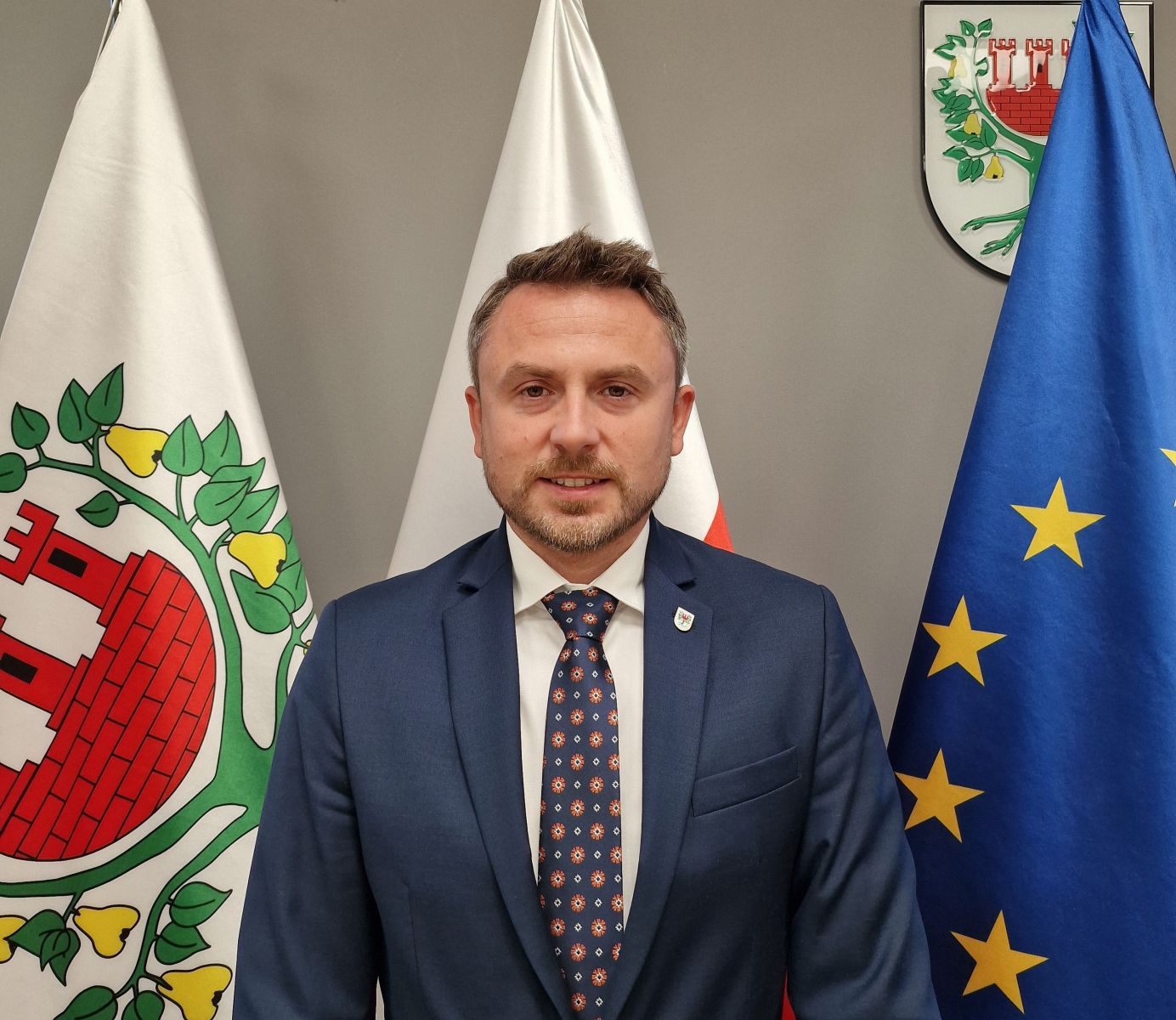 na zdjęciu Zatępca Burmistrza na tle flag Międzychodu, Polski i UE